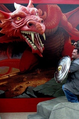 A photo of Eddie with a sword and shield looking at a cardboard dragon