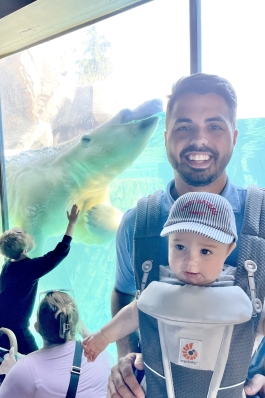 Andrew Cantrell with a baby in a carrier strapped to his chest, in front of a live polar bear exhibit