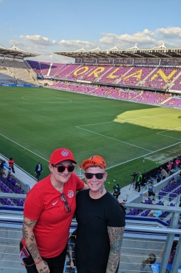 A photo of Lori and her partner with the Orlando City SC field in the background.