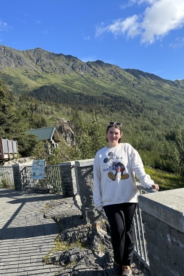 Eve standing on a viewpoint, with a picturesque view of Anchorage's mountains.
