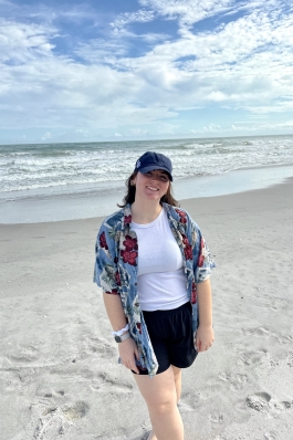 Eve standing in front of a beach with white sand and a clear blue sky.